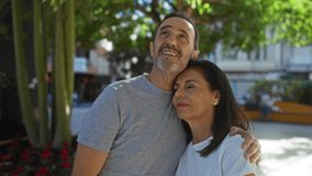 Middle-aged hispanic couple embracing lovingly outdoors in a sunny urban park setting, capturing warmth, happiness, and companionship in an idyllic city environment. - Powered by Shutterstock - Get 15% off with code: PIKWIZARD15