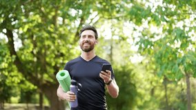 Sportsman engages in fitness by walking in park with yoga mat and water bottle, checking phone for workout updates. Smiling bearded athletic returning from training. Active lifestyle, healthy routine - Powered by Shutterstock - Get 15% off with code: PIKWIZARD15