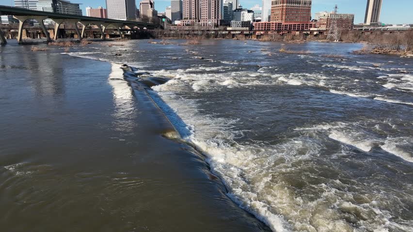 Splashing water of James River in front Richmond skyline. Sunny day in spring season. Aerial low angle shot. Skyscraper, bridge and towers in background.