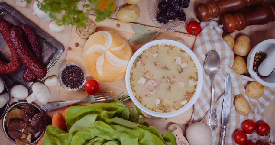 Close-up of sour rye soup surrounded by cold cuts and vegetables.