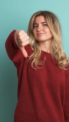 Sad young woman showing thumb down in blue studio