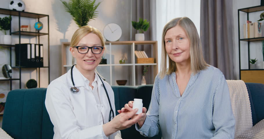 Women doctor and patient sitting in front of camera with sincerely smiles and holding bottle with vitamins. Healthcare concept