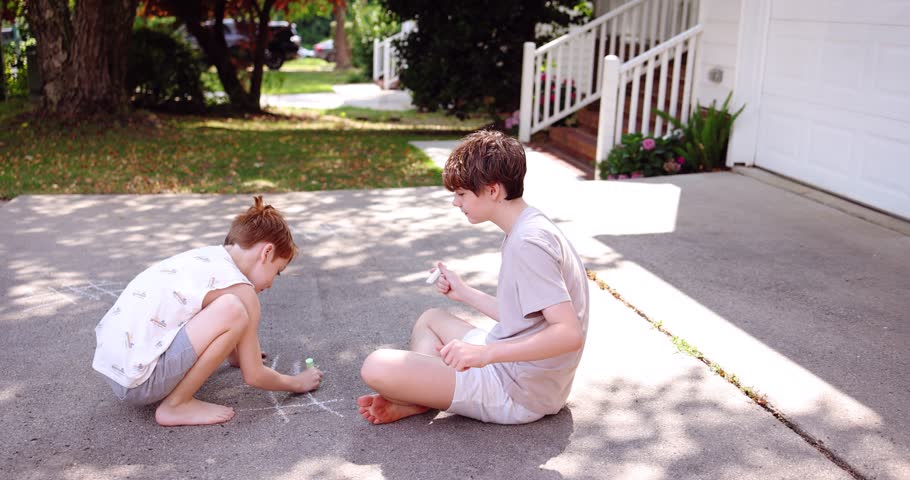 Two Brothers Playing Tic Tac Toe with Sidewalk Chalk on a Suburban Driveway – Peaceful Summer Day. A cozy family lifestyle moment capturing bonding and outdoor play under natural light.