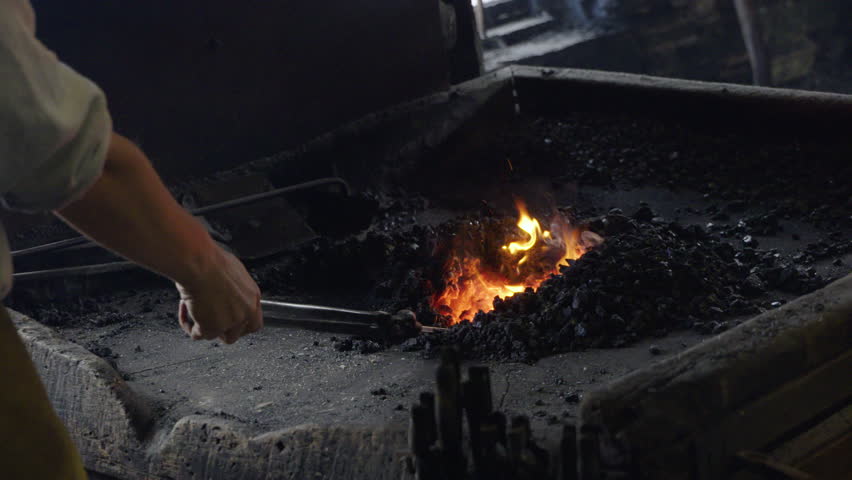 Metal rod being taken from fire and hammered on anvil