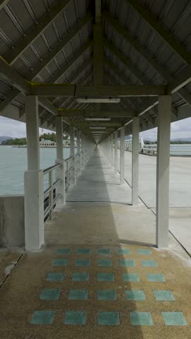 A long, covered pier stretches over the water, creating a stunning perspective effect with its symmetrical roof structure and supporting pillars. The converging lines of the walkway lead toward a