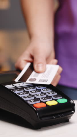 Vertical Format Video of Close up of woman hands making payment with credit card machine terminal while swiping debit card to pay the bill. NFC credit card payment. Wireless money transaction.