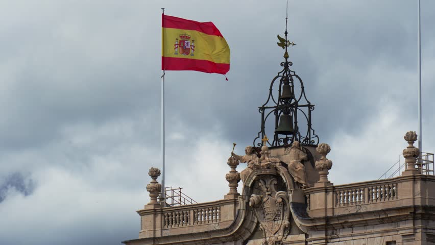 Spanish flag waving on royal palace of madrid rooftop on cloudy day