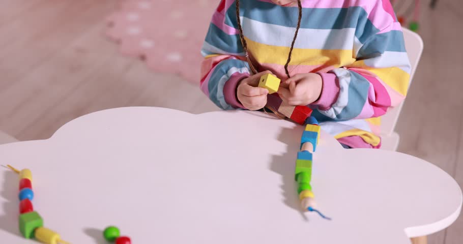 Motor skills development. Little girl playing with threading toy at white table indoors, closeup