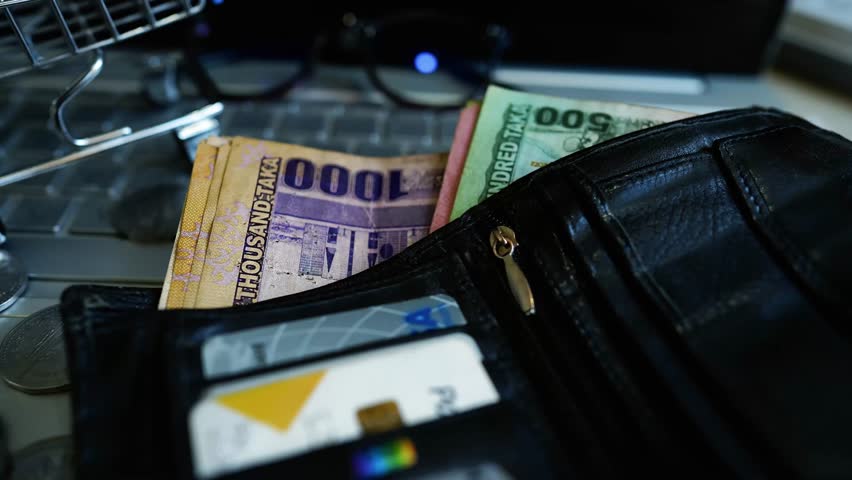 Wallet with Bangladeshi Taka on Laptop Keyboard, A wallet containing Bangladeshi Taka notes and credit cards is placed on a laptop keyboard