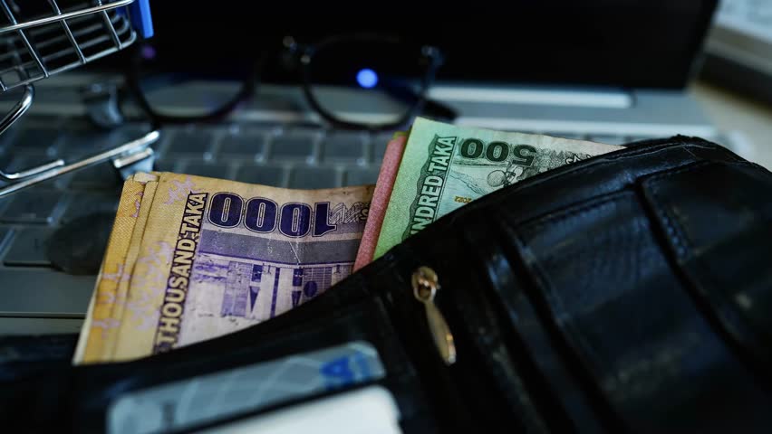 Wallet with Bangladeshi Taka on Laptop Keyboard, A wallet containing Bangladeshi Taka notes and credit cards is placed on a laptop keyboard