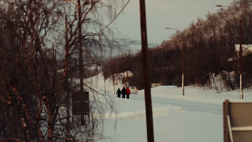 People walking down snowy road out of Kilpisjarvi in northern Finland, graded.
