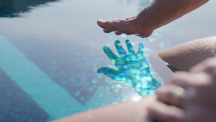A hand glides gracefully through crystal-clear pool water in slow motion, creating gentle ripples that shimmer under the sunlight
