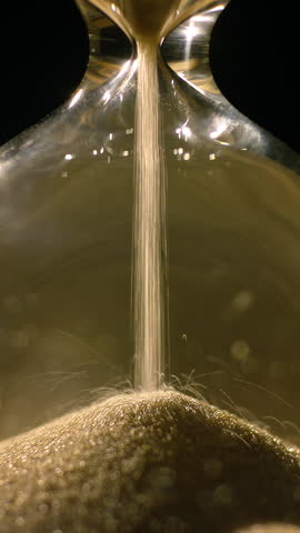 Vertical video of Golden sand leaking through the hourglass, measuring the passage of time, extreme close up shot. Deadline, moment, and evanescence concepts.