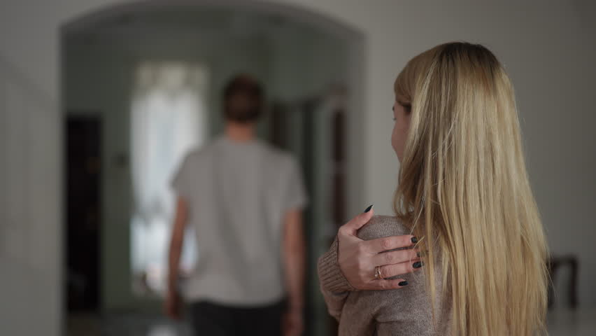 In slow motion, a man in a gray shirt turns and walks away after insulting his wife. The woman, with blonde hair, stands with a worried expression, one hand on her shoulder, as she watches him leave - Powered by Shutterstock - Get 15% off with code: PIKWIZARD15