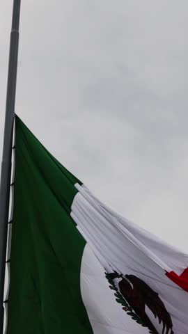 mexican flag waving in front of the cathedral in merida yucatan mexico on a cloudy overcast day in latin america (beautiful colonial spanish style architecture with mayan stones)