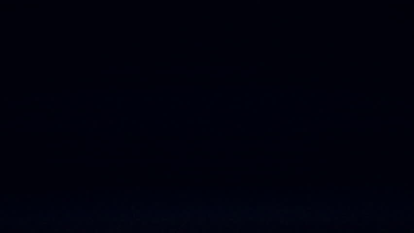 Blurred streaks of glowing urban lights stretch across the night, with vivid hues of red, blue, and white appearing on the screen