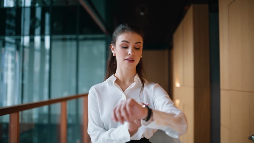 Rich business woman walking office corridor wearing elegant white blouse closeup. Successful businesswoman checking time on hand watch hurrying on meeting. Smiling female boss going on modern hallway.