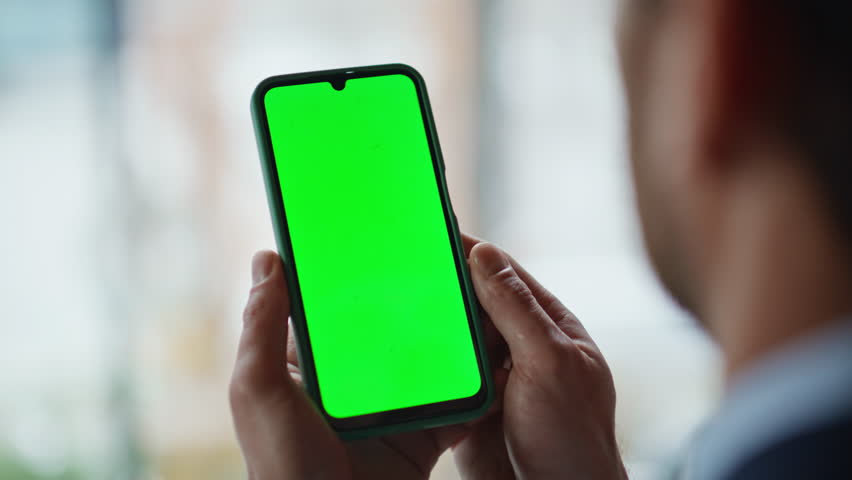 Businessman hands holding greenscreen cellphone at office closeup. Unknown business manager browsing app at mockup smartphone at workplace. Successful executive reading message on chroma key phone.