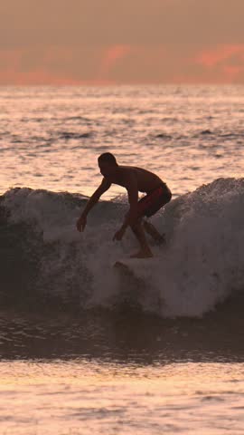 A silhouette of male surfer riding an ocean wave during a stunning sunset.Indian ocean.Vertical video