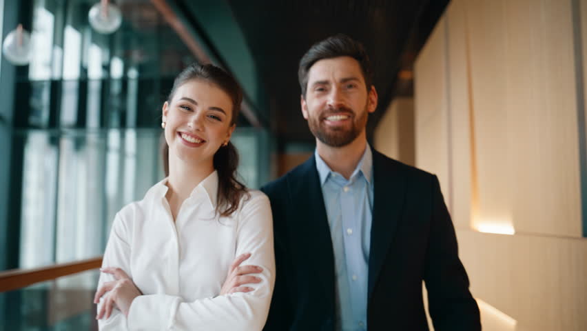 Confident business people walking corporate corridor closeup. Successful two partners smiling pointing finger to camera on go. Happy woman man colleagues posing together at modern office hallway.