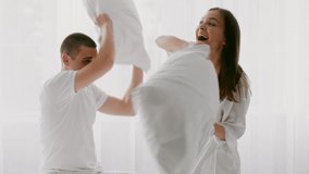A young couple in a bright bedroom engages in a playful pillow fight. Their laughter fills the air as they share a moment of joy and affection together, creating a warm atmosphere. - Powered by Shutterstock - Get 15% off with code: PIKWIZARD15
