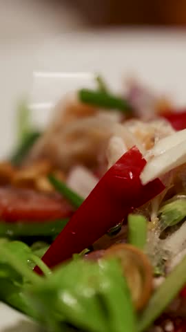 A colorful Thai salad with fresh greens, chili, and noodles, captured in a close-up with soft lighting