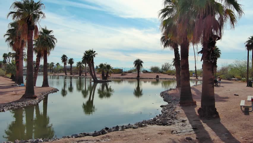 aerial footage of a gorgeous landscape at Papago Park with a lake, lush green palm trees and rocks in Phoenix Arizona USA