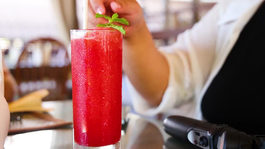 A person prepares a vibrant watermelon juice in a cozy Thai cafe, highlighting fresh ingredients and a relaxed atmosphere