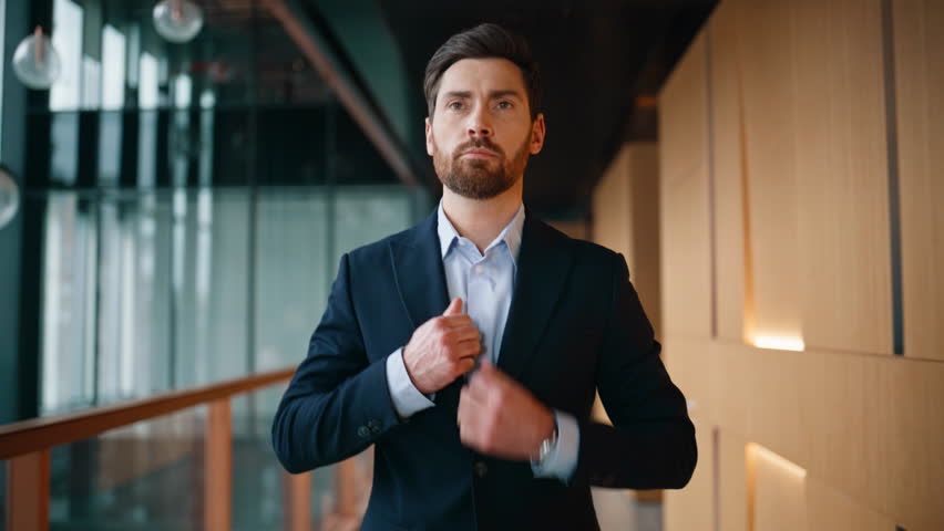 Wealthy man buttoning jacket walking modern office interior closeup. Confident businessman checking time at handwatch hurrying on business meeting. Elegant executive going at contemporary hallway.