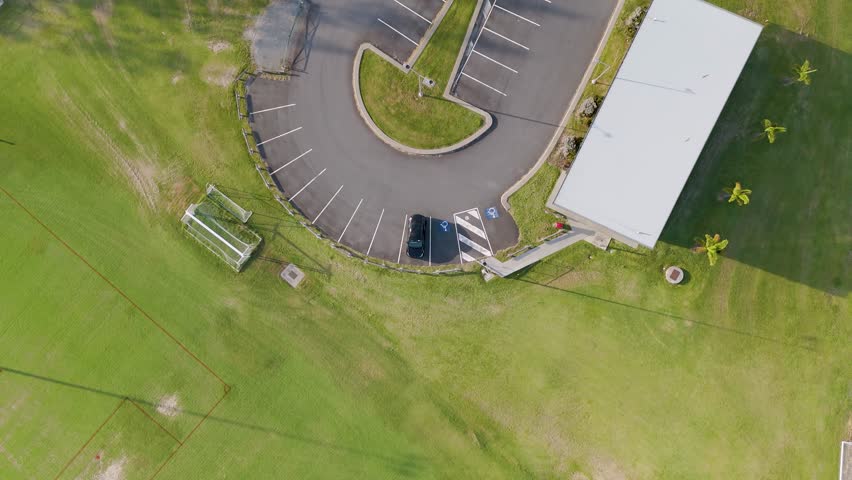 Drone footage captures a soccer field and adjacent carpark under bright daylight, showcasing the layout and surrounding greenery