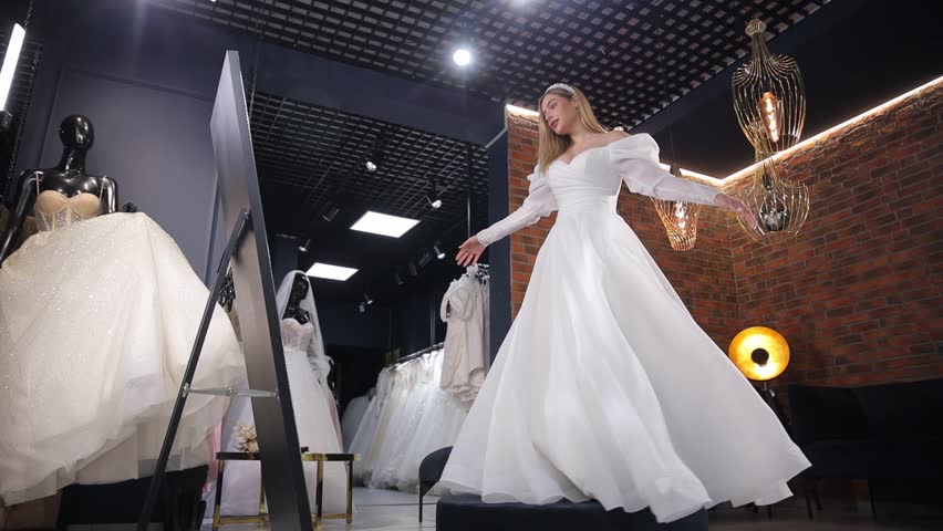 Attractive young bride posing in front of a mirror while choosing a wedding dress