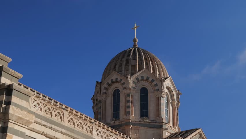 The ornate dome of Notre-Dame de la Garde Basilica in Marseille stands against a vivid blue sky. Featuring striped stone patterns and a golden cross, this iconic landmark symbolizes faith and history