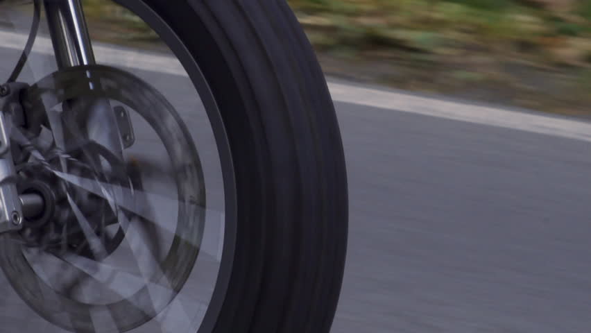 Close up of motorcycle front wheel spinning at high speed in slow motion. Low angle chase car shot in slow motion with blur. Camera movement, moody tones.