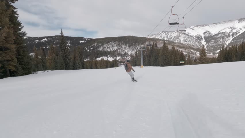 Rear view of snowboarding riding down Copper Mountain during evening at Colorado, USA.