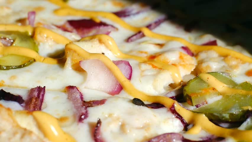 Italian pizza close up. Slow motion, mouth watering pizza fresh baking , featuring melted cheese, chicken, red onions, pickles, and a drizzle of mustard. Macro shoot of pizza. 