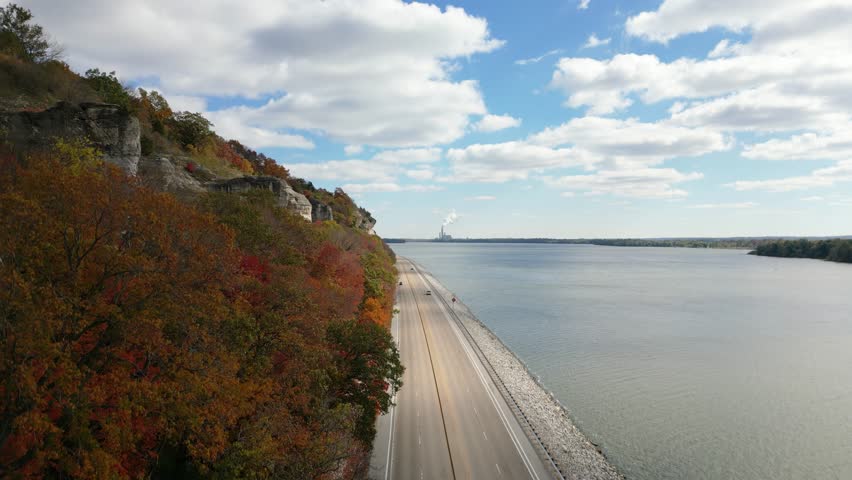 Rising drone shot of the Mississippi River Bluffs along the Great River Road in Illinois. The trees are displaying their autumn colors under a sunny blue sky.
