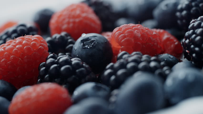 Fresh and colorful raspberries blueberries and blackberries are seen in a close up shot with water droplets Perfect for food and healthy eating content