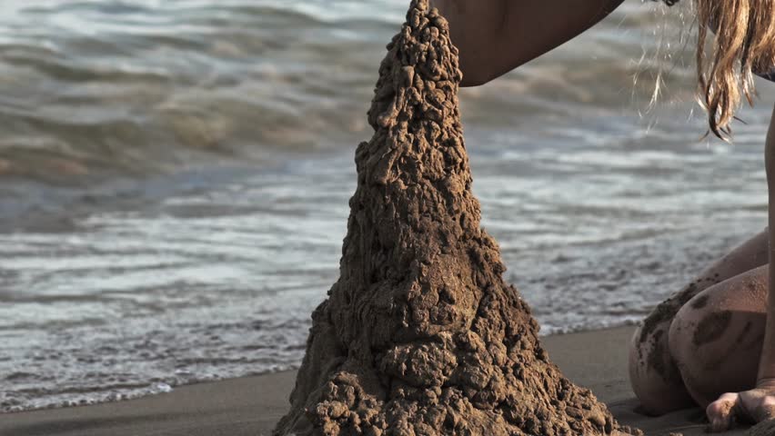 Young girl builds sandcastle from damp sand on seaside shore, close-up view. Child enjoys outdoor play. Family getaway. Joyful moments of childhood. Vacation destination. Travel and leisure theme