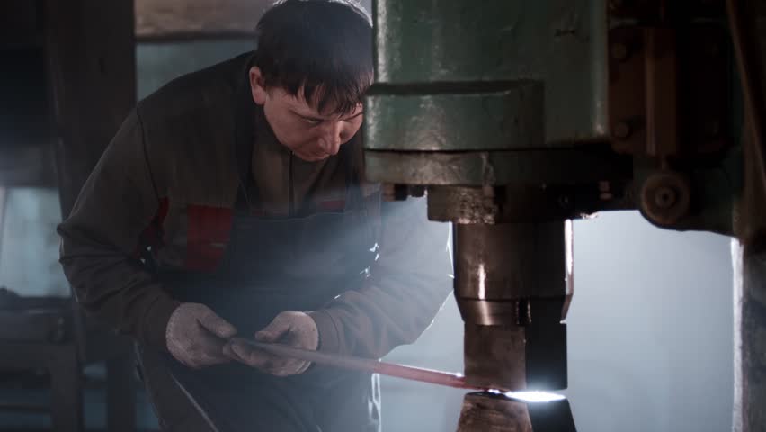 Blacksmith forging metal with power hammer in workshop