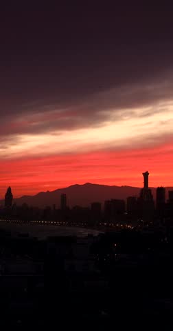Portrait vertical footage of the sun setting in the evening over the old town of Benidorm in Spain showing the beautiful red sun set with clouds in the sky along side high rise apartments building