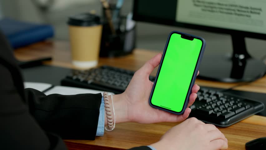 Young Woman In Glasses Using Mobile Phone With Green Screen Mock Up In Office. Smartphone In Hands Close Up
