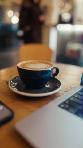 Intimate CloseUp View of a Coffee Cup and Laptop by a Window in a Cozy, Inviting Cafe Setting for Work or Relaxation