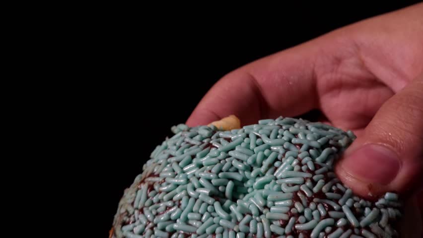 A close-up shot of a chocolate mint donut being ripped in half by hand, revealing its soft, airy texture. The glossy mint green chocolate coating contrasts beautifully with the dark background