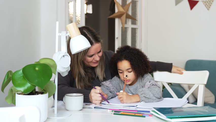 Caucasian mother and African American daughter studying at home, doing homework in cosy white room. Parent teach, child school girl learn knowledge, write exercise read book. Education for children