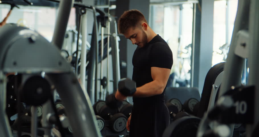 Sportsman doing workout indoors. Muscular shirtless athlete is lifting dumbbells in hands at sports gym