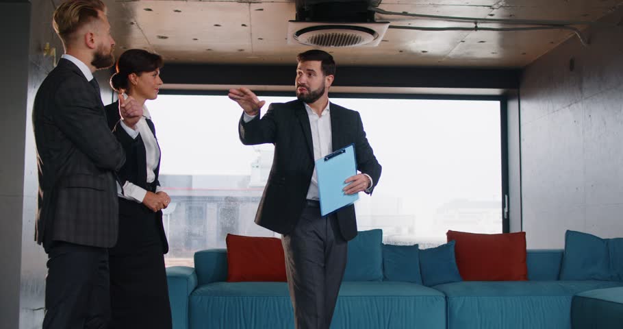 Potential buyers looking at interior of new office building. Realtor with clipboard giving office tour to people who plan purchasing or renting business premises. Commercial real estate concept