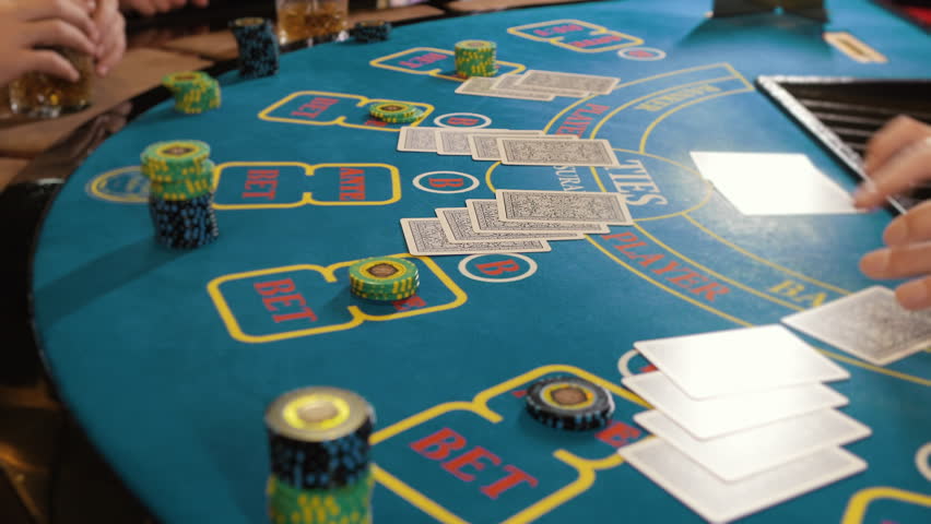 Close up of dealer hands dealing cards on baccarat table with chips in casino atmosphere, elegant gambling scene indoors.