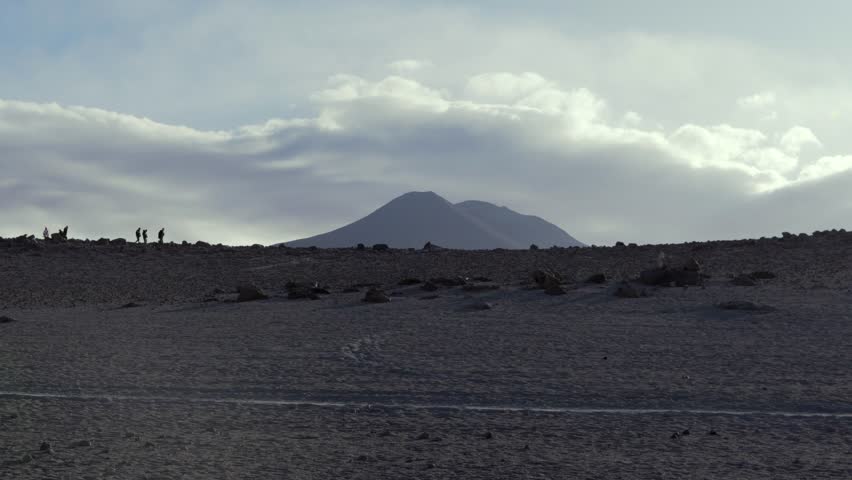 Establishing static of Laguna Colorada in Bolivia Sud Lipez, as hikers walk along ridge with mountain volcano in backdrop