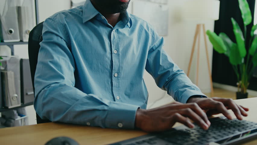 Tired African American man massaging his neck. Stretching muscles while feeling exhausted after long work session in bright modern office. Having pain in his back. Rubbing head with one hand.