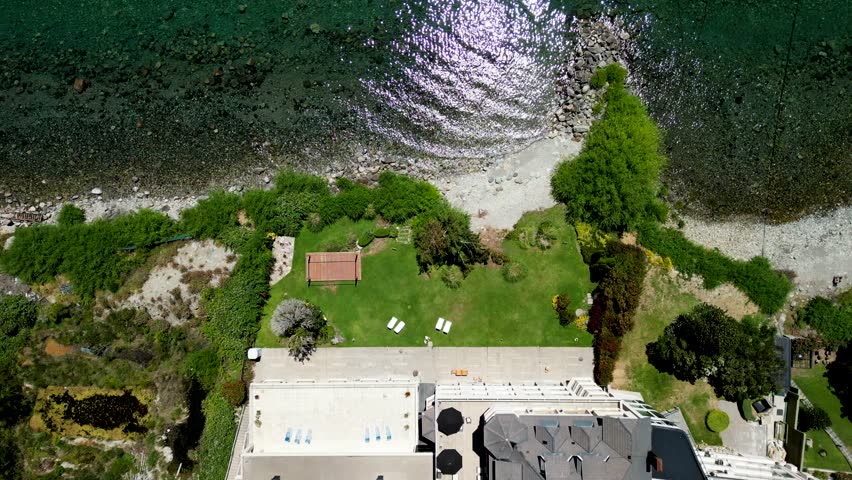 4K drone footage of a lakeside hotel in Bariloche, Patagonia, in summer. Scenic Lake Nahuel Huapi, lush greenery, and Andes mountains under a sunny sky. Perfect for travel or luxury projects.